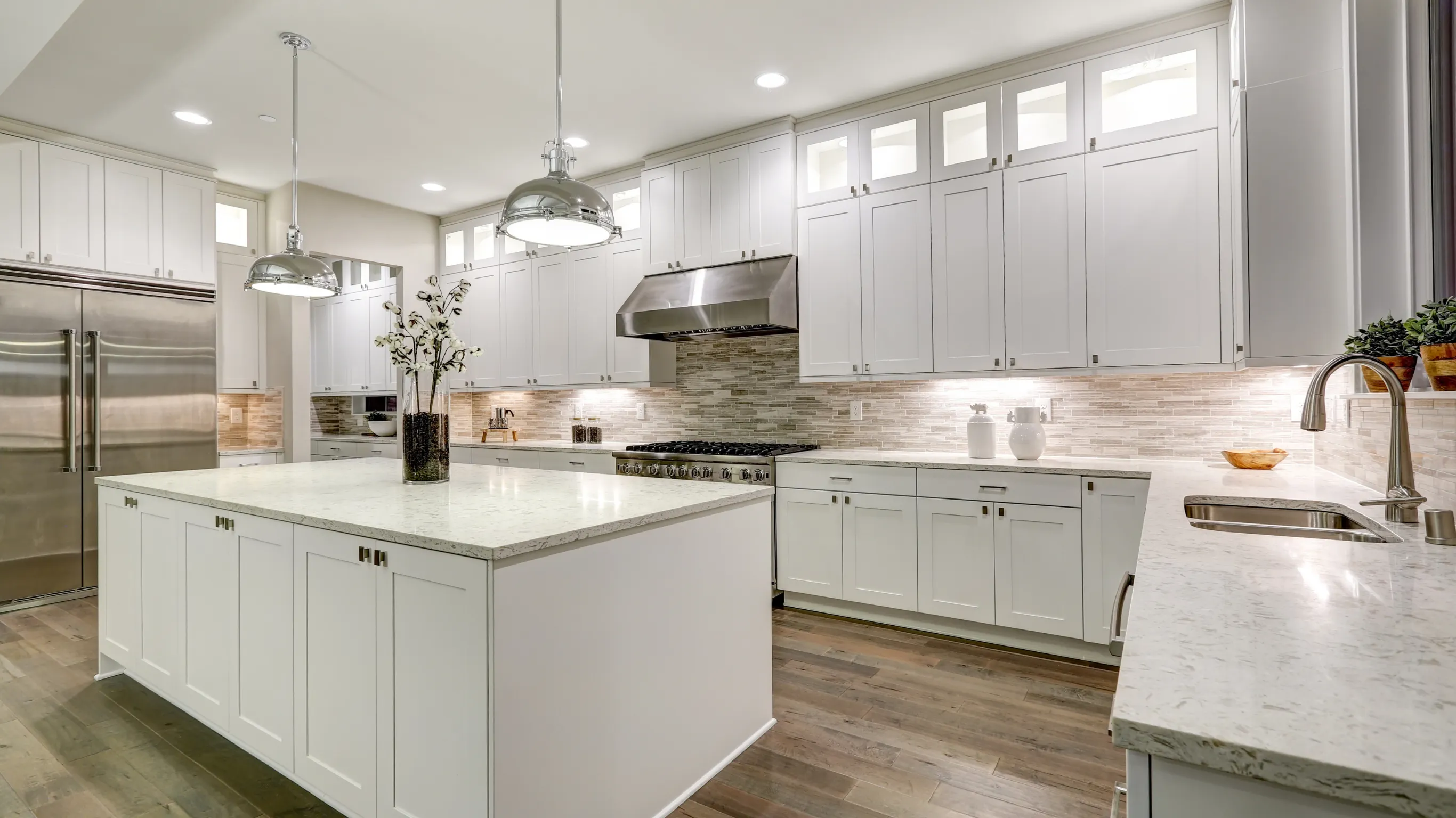After kitchen remodeling project in Los Angeles featuring white custom cabinets, quartz countertops, pendant lighting, tile backsplash, and a large island.
